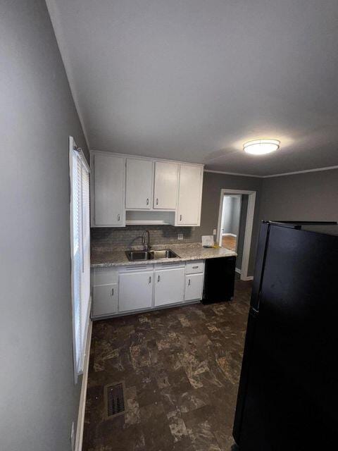 kitchen featuring decorative backsplash, sink, black fridge, and white cabinetry