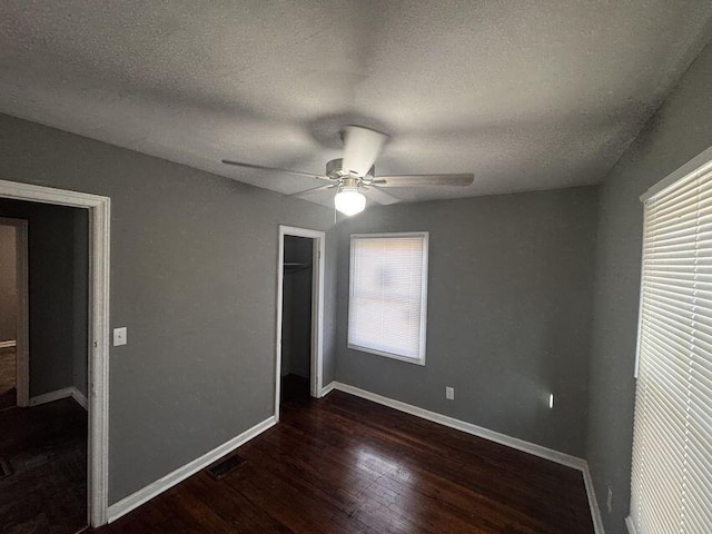 unfurnished bedroom with ceiling fan, a closet, a textured ceiling, and dark hardwood / wood-style floors