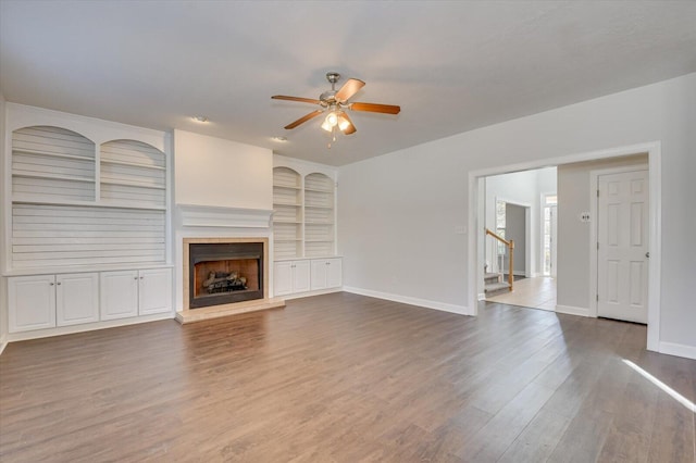 unfurnished living room with ceiling fan, wood-type flooring, and built in features