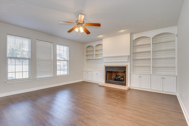 unfurnished living room featuring ceiling fan, built in shelves, and wood-type flooring