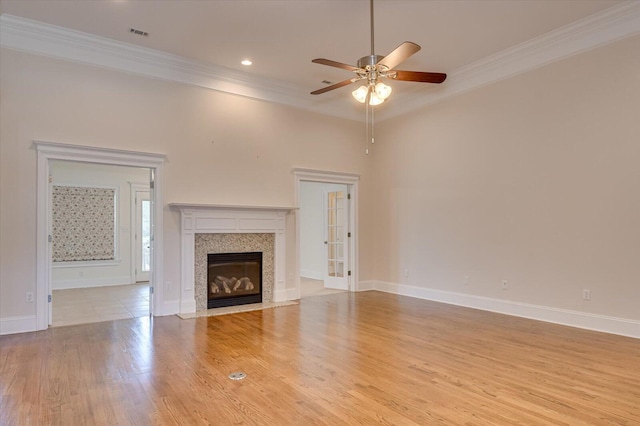 unfurnished living room featuring a high end fireplace, light hardwood / wood-style floors, ceiling fan, and ornamental molding