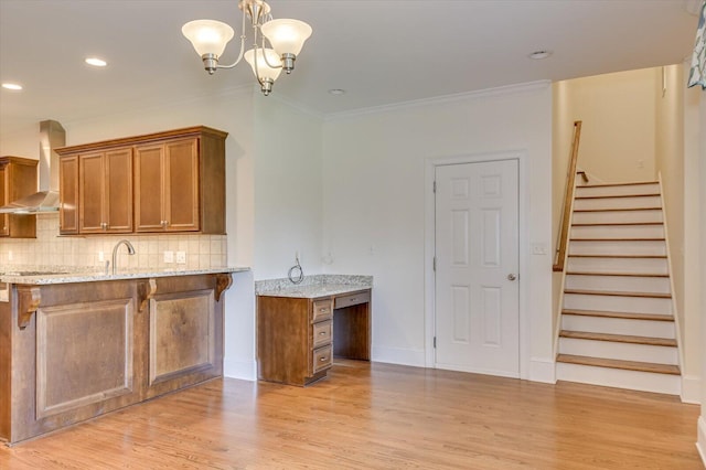 kitchen with crown molding, light hardwood / wood-style flooring, wall chimney exhaust hood, light stone countertops, and kitchen peninsula