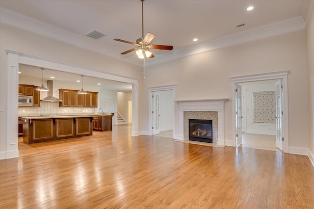 unfurnished living room featuring crown molding, a high end fireplace, light wood-type flooring, and ceiling fan