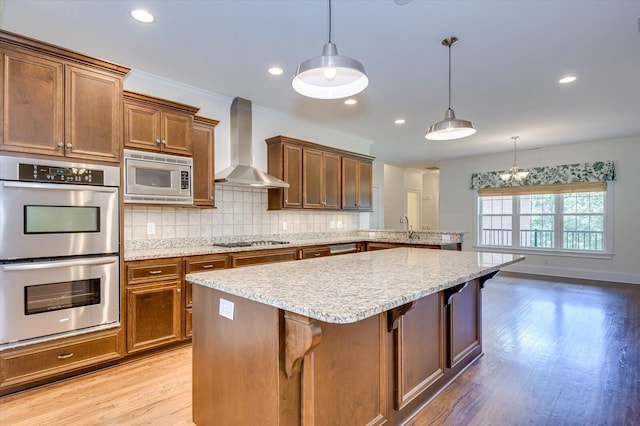 kitchen with a kitchen breakfast bar, wall chimney range hood, stainless steel appliances, and hanging light fixtures