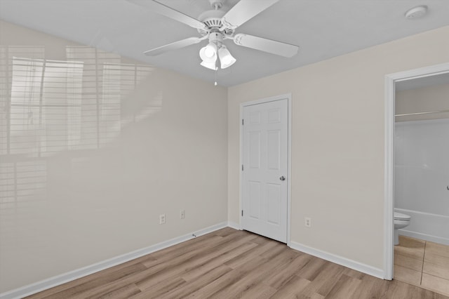 unfurnished bedroom with baseboards, ensuite bath, wood finished floors, and ceiling fan