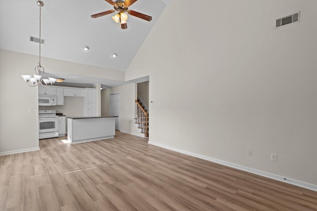 unfurnished living room with high vaulted ceiling, light wood finished floors, visible vents, and stairway