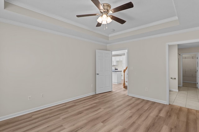 unfurnished bedroom with baseboards, crown molding, a tray ceiling, and light wood finished floors