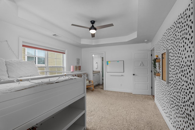 bedroom with a raised ceiling, light colored carpet, and ceiling fan