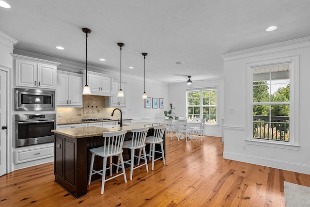 kitchen featuring stainless steel appliances, an island with sink, crown molding, a kitchen bar, and white cabinetry