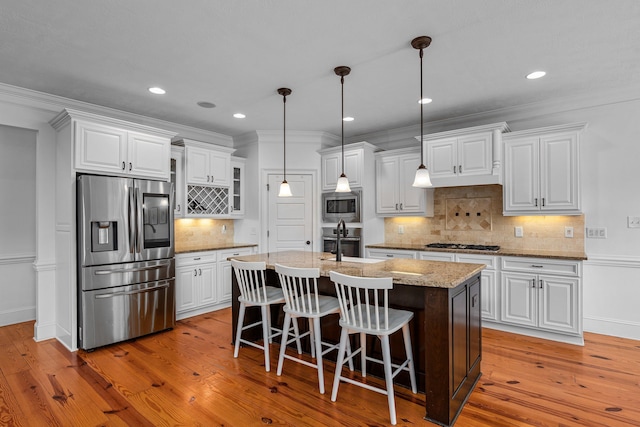 kitchen with stainless steel appliances, white cabinets, an island with sink, a breakfast bar area, and pendant lighting