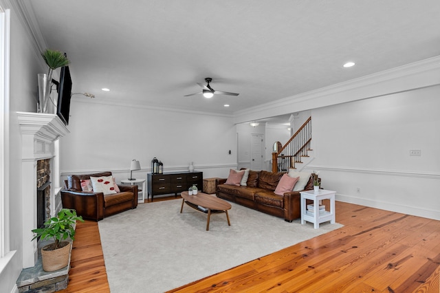 living room with hardwood / wood-style flooring, ceiling fan, crown molding, and a stone fireplace