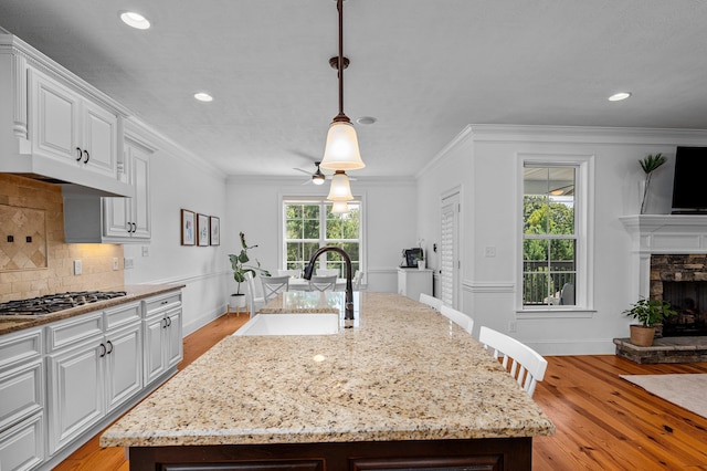 kitchen featuring a center island with sink, stainless steel gas stovetop, a fireplace, ceiling fan, and sink