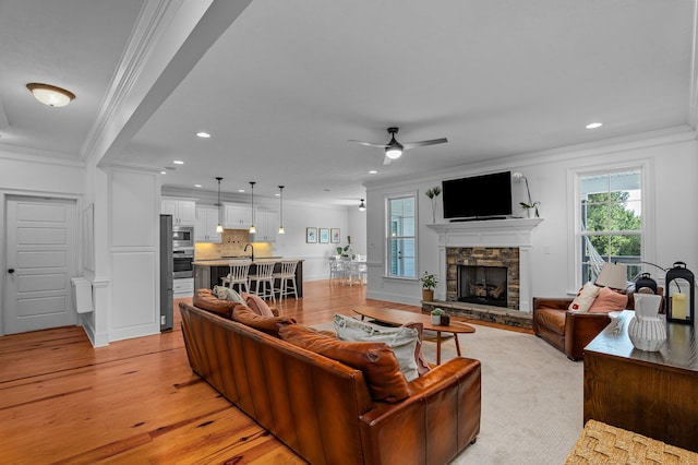 living room featuring a fireplace, light wood-type flooring, ceiling fan, and crown molding