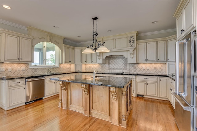 kitchen with appliances with stainless steel finishes, an island with sink, light wood-style flooring, a sink, and ornamental molding
