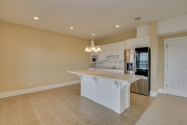 kitchen featuring stainless steel fridge, light countertops, a kitchen breakfast bar, white cabinets, and a sink