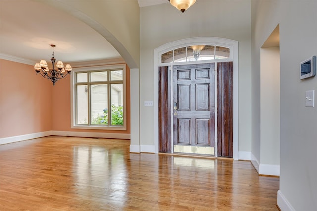 entrance foyer featuring a chandelier, arched walkways, baseboards, and light wood-style floors