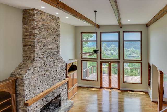 unfurnished living room featuring a stone fireplace, light wood-style floors, a ceiling fan, beam ceiling, and baseboards