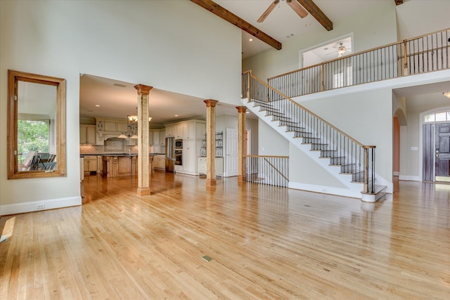 unfurnished living room featuring a high ceiling, ceiling fan, light wood finished floors, stairway, and arched walkways