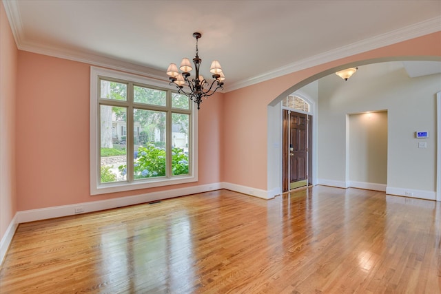 spare room featuring arched walkways, a chandelier, light wood finished floors, baseboards, and crown molding