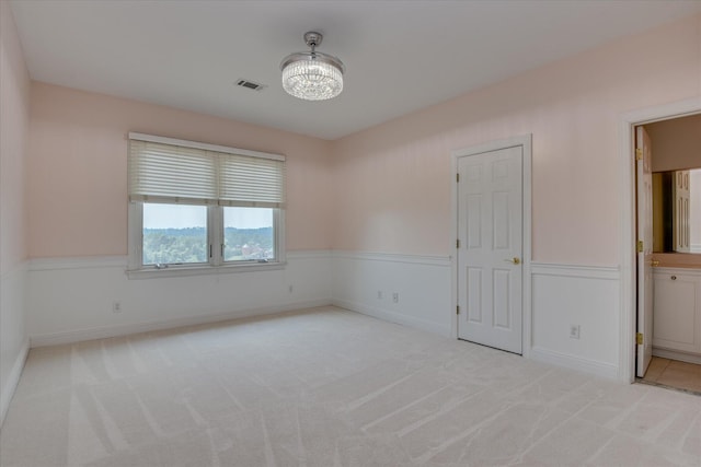 unfurnished room featuring light colored carpet, wainscoting, and a chandelier
