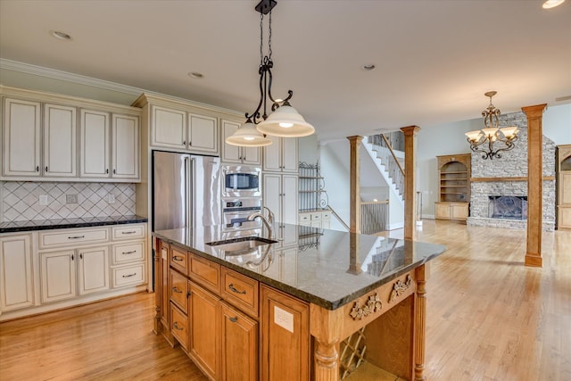 kitchen with a sink, appliances with stainless steel finishes, cream cabinets, backsplash, and light wood finished floors