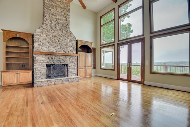 unfurnished living room with a high ceiling, wood finished floors, a stone fireplace, plenty of natural light, and ceiling fan