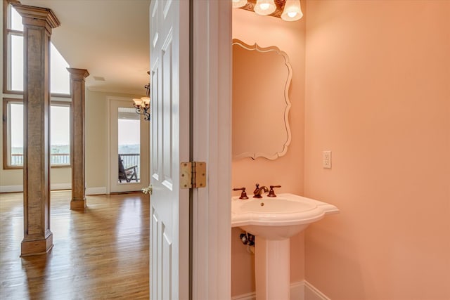bathroom featuring decorative columns, a chandelier, wood finished floors, baseboards, and ornamental molding