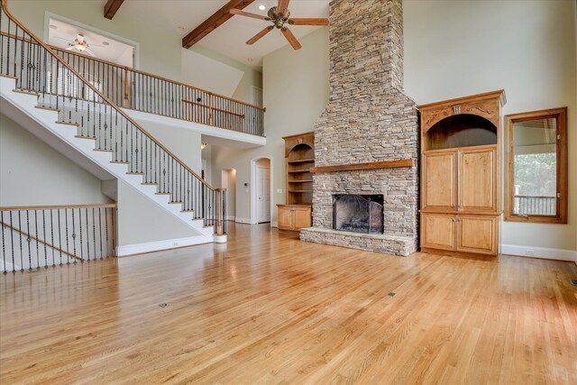unfurnished living room featuring ceiling fan, a towering ceiling, light wood finished floors, a fireplace, and baseboards