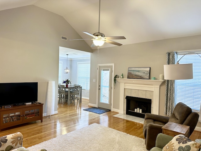 living area with ceiling fan, a tile fireplace, light wood-style flooring, visible vents, and baseboards