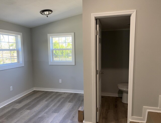 unfurnished bedroom with connected bathroom, a spacious closet, wood-type flooring, and vaulted ceiling