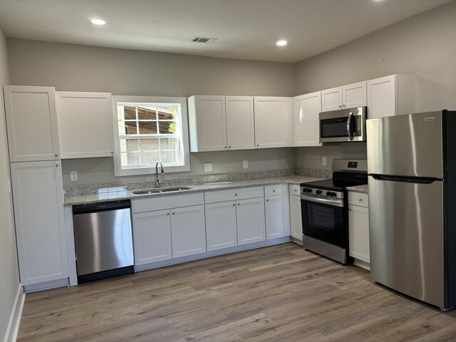 kitchen featuring appliances with stainless steel finishes, light wood-type flooring, light stone counters, sink, and white cabinets