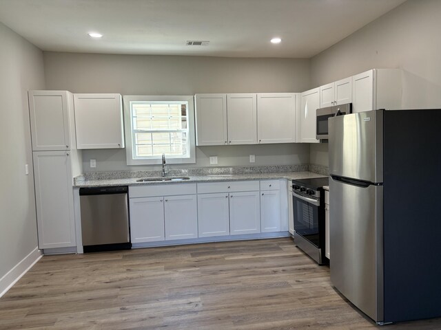 kitchen featuring light stone countertops, white cabinetry, sink, light hardwood / wood-style flooring, and appliances with stainless steel finishes