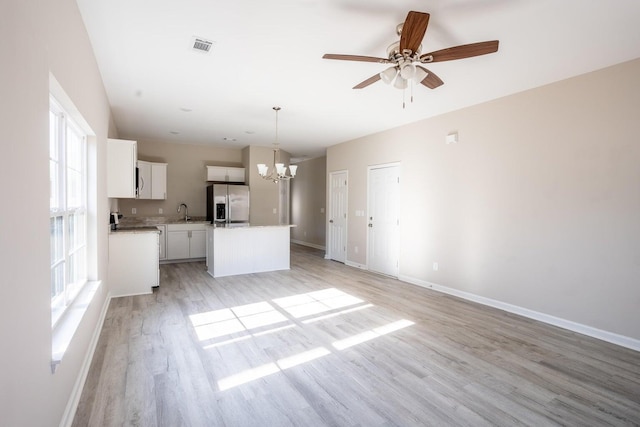 unfurnished living room featuring ceiling fan with notable chandelier, a wealth of natural light, and light hardwood / wood-style flooring