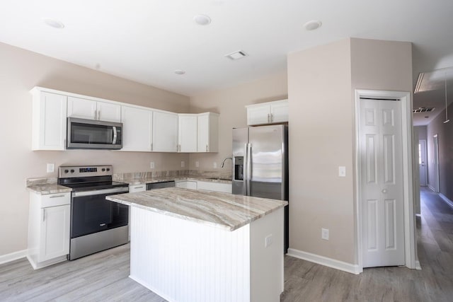 kitchen with light stone counters, white cabinetry, appliances with stainless steel finishes, and a kitchen island