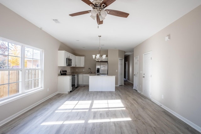 kitchen with pendant lighting, white cabinets, a center island, stainless steel appliances, and light wood-type flooring