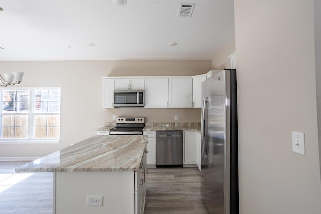 kitchen with white cabinetry, appliances with stainless steel finishes, light wood-type flooring, light stone counters, and a center island