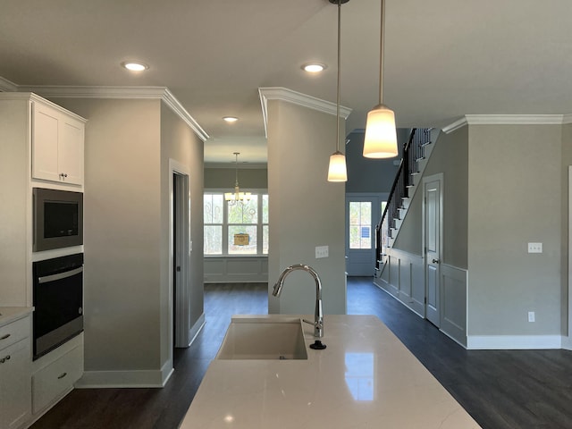 kitchen with built in microwave, stainless steel oven, sink, pendant lighting, and white cabinets