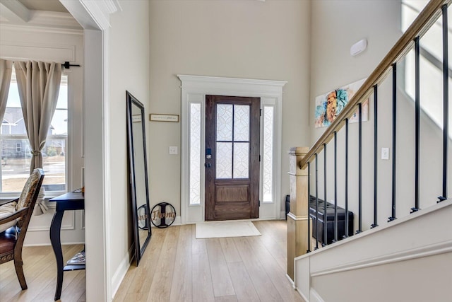 entrance foyer with light wood finished floors, baseboards, stairway, and ornamental molding