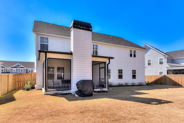 rear view of property featuring a yard, a shingled roof, a chimney, and a fenced backyard