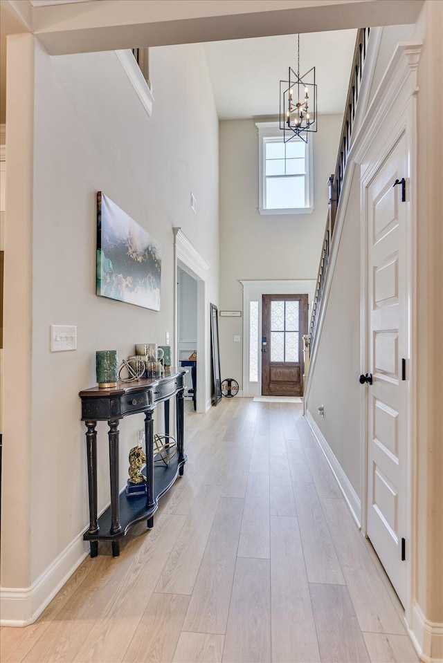 foyer entrance featuring baseboards, light wood finished floors, stairway, and a notable chandelier