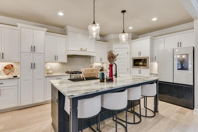 kitchen featuring white cabinetry, a kitchen breakfast bar, freestanding refrigerator, range hood, and stainless steel microwave