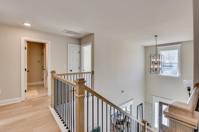 corridor featuring visible vents, light wood-type flooring, an upstairs landing, and baseboards