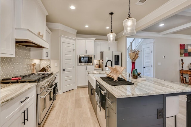 kitchen featuring light wood finished floors, white refrigerator with ice dispenser, a center island with sink, stainless steel microwave, and white cabinetry