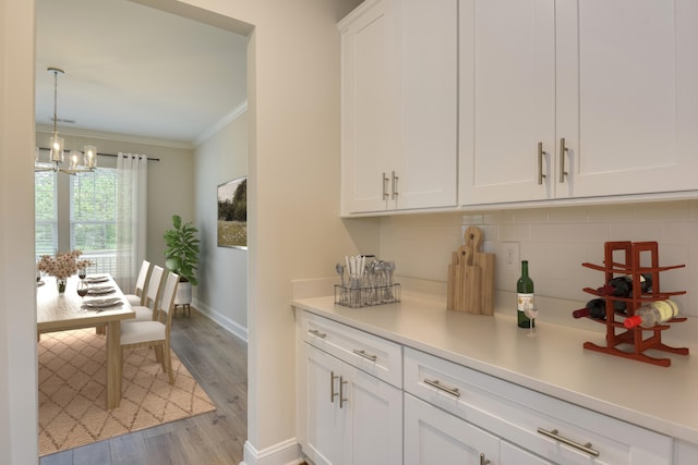 kitchen with wood finished floors, white cabinetry, crown molding, light countertops, and decorative backsplash