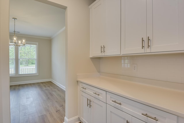 interior space with light wood-type flooring, ornamental molding, backsplash, a chandelier, and hanging light fixtures