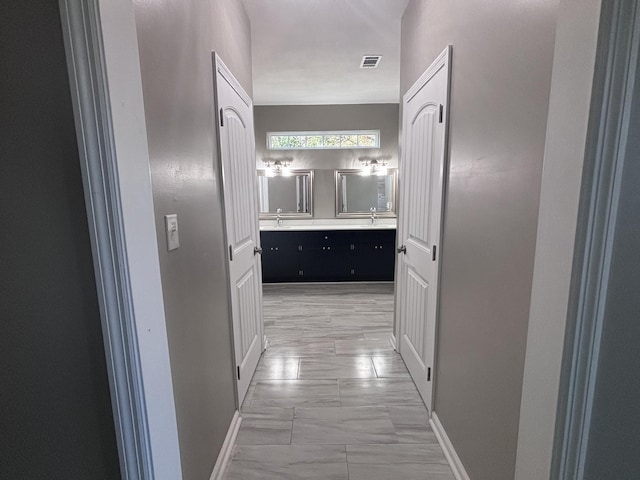 hall featuring a sink, visible vents, baseboards, and marble finish floor