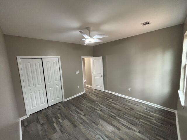 unfurnished bedroom with a ceiling fan, baseboards, visible vents, dark wood-type flooring, and a closet