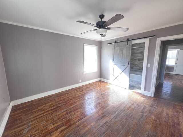 unfurnished bedroom featuring a barn door, ceiling fan, dark wood-type flooring, and ornamental molding