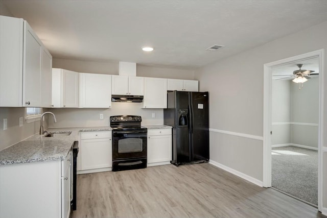 kitchen with white cabinets, light stone counters, a sink, under cabinet range hood, and black appliances