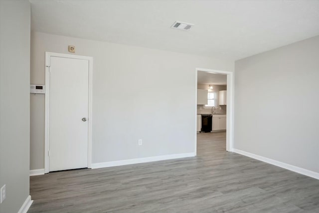 unfurnished room featuring visible vents, a sink, light wood-style floors, and baseboards